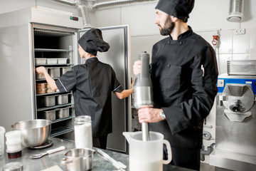 Chef cook with young woman assistant making ice cream together mixing ingredients in the professional kitchen of the small manufacturing