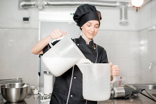 Young woman chef pouring milk prepairing basis for ice cream production in the kitchen