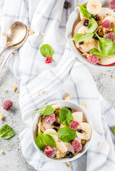 Healthy summer breakfast, fruit and berry salad with spinach, granola, apple and banana, white marble background