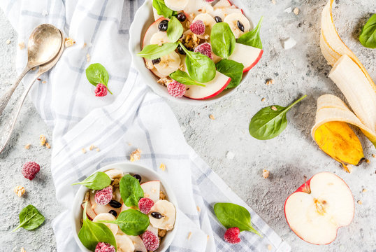 Healthy summer breakfast, fruit and berry salad with spinach, granola, apple and banana, white marble background