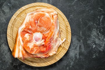 Raw ham cut on a round cutting board on a black cement background, top view with copy space