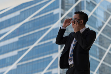 Young Asian businessman sweating due to hot climate. He wiping the face with wet wipes, perspiration, sweat in a city Bangkok Thailand.