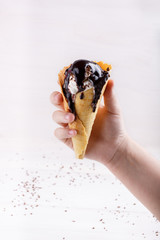 Homemade vanilla ice-cream with chocolate topping in waffle cone held in the hand on white.