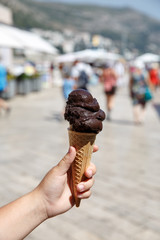 Hand holding dark chocolate ice-cream in waffle cone over blurred street city background