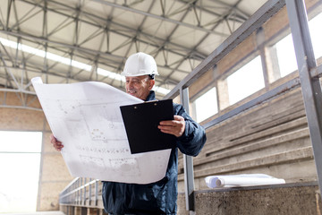 Senior construction manager controlling building site with blueprints.