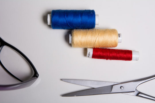 Three coils of multicolored threads, glasses and scissors