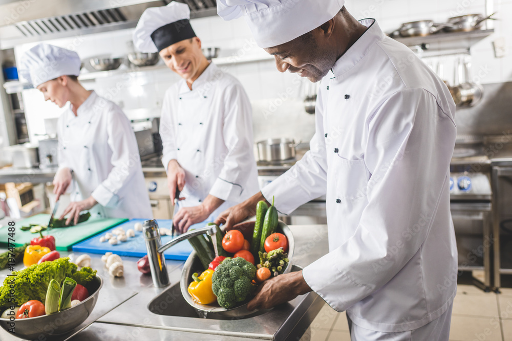 Wall mural smiling african american chef washing vegetables at restaurant kitchen