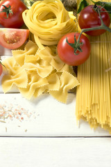 Dry pasta with vegetables on white wooden table.