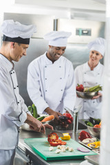 happy multicultural chefs preparing vegetables at restaurant kitchen