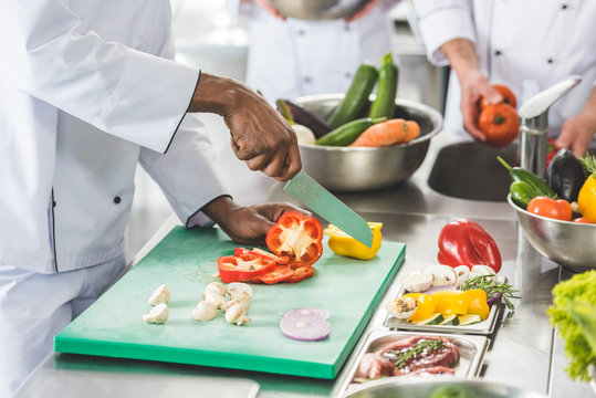 cropped image of multicultural chefs cutting and washing vegetables at restaurant kitchen