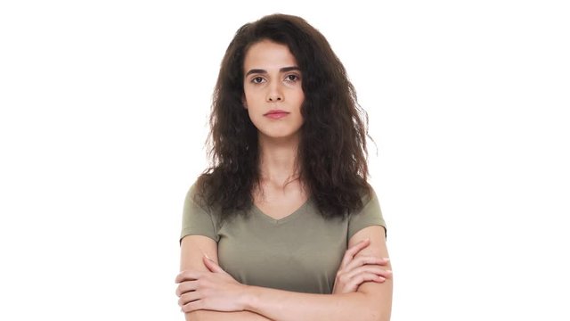 Indoor portrait of persistent caucasian woman with dark curly hair holding index finger on lips asking to keep silence while saying shh, over white background. Concept of emotions