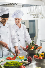 chef watching how colleague cutting vegetables at restaurant kitchen