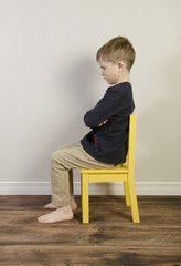 An angry little boy sits on a yellow time out chair © wendyhayesrise