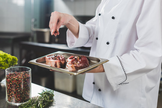 cropped image of chef adding spices to raw steaks at restaurant kitchen