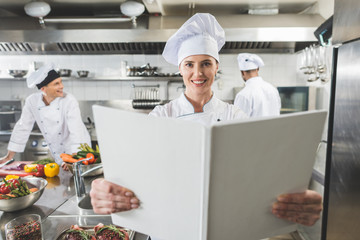 happy chef holding recipe book at restaurant kitchen