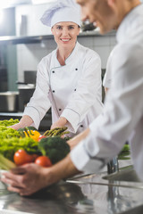 smiling chefs with vegetables at restaurant kitchen