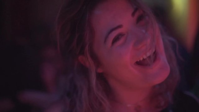 Slow motion shot of attractive millennial woman smiling flirtatiously into camera as she dances in night club