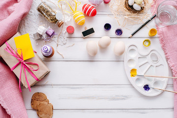 Fototapeta na wymiar Top view of handmade easter objects laying on white wooden desk, daughter's hands painting, decorate eggs, holding brushed. Day before Easter, child painting eggs for Easter