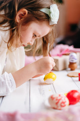 Obraz na płótnie Canvas Smile girl colours eggs for Easter at home. Easter objects, things, laying on white wooden table, daughter's hands painting, decorate eggs, holding brushed