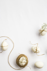 Easter eggs are minimalistically decorated with twine and gypsophila flowers. On a white background with a brown rope. Top view, flat lay