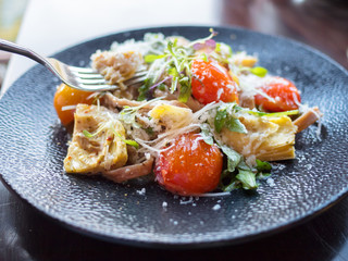 Artichoke and tomato salad with cheese on dark plate over a wooden table