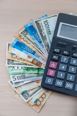Different banknotes of different denominations are stacked in a fan and a calculator on the table vertically.