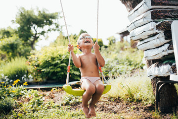 lachender farbiger Junge schaukelt im Garten im Sommer