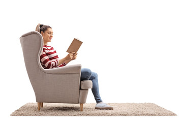 Young woman seated in an armchair reading a book