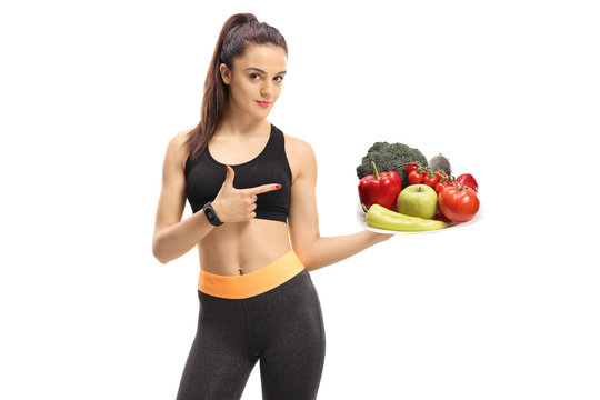 Fitness woman holding a plate of vegetables and fruit and pointing