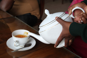 Hands of an Asian woman holding a large white kettle and pouring tea into a cup, Sri Lanka
