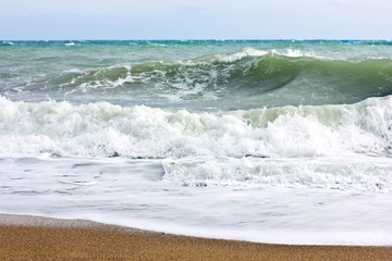 Stormy sea and blue sky, white sea foam on a yellow sandy beach.