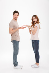 Full length photo of puzzled adult guy and girl wearing beige t-shirts standing face to face and gesturing on each other with claims, over white background