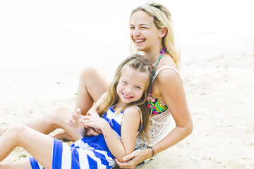 Young blonde mother cuddles and is playing with her daughter on the beach and havin fung
