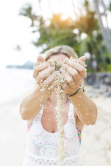 Fototapeta premium young pretty woman lets sand trickle from her hands an a beautiful beach in thailand