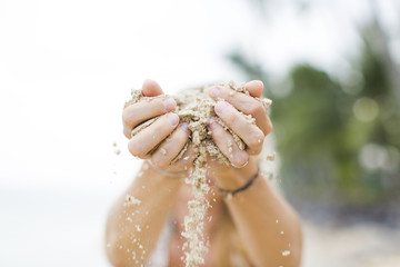 young pretty woman lets sand trickle from her hands an a beautiful beach in thailand