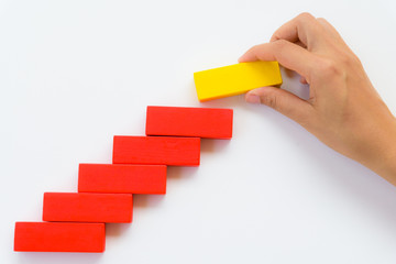 Concept of building success foundation. Women hand put yellow wooden block on red wooden blocks in the shape of a staircase