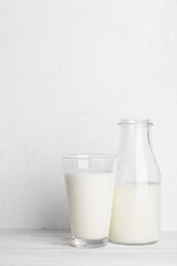 Bottle of milk ang glass of milk on white wooden table background vertical with copy space