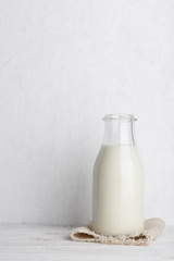Bottle of milk on a sack cloth on white wooden table background vertical with copy space