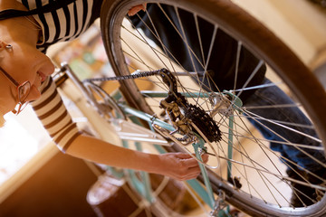 Beautiful cheerful woman checking bicycle wires in the sunny garage.