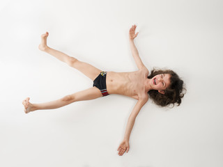 Long-haired little boy in a swimsuit lying on his back, isolated on a light