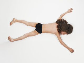 Adorable little boy in bathing suit lying on stomach with arms outstretched, isolated on light