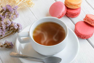 Different types color of macaroons with Cup of hot tea on white wooden background