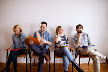 Group of upset and bored young people sitting in a row in the waiting room with a folder in hand before an interview with the entrepreneur.