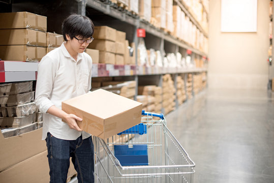 Young Asian man putting paper box into trolley cart in warehouse, shopping warehousing concept