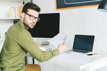 Thoughtful young man by working table with computers at home office