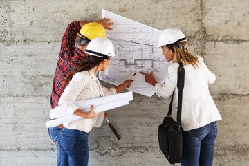 Team of inspectors and architects discuss about blueprints on construction site.