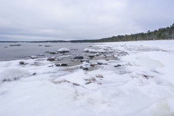 Old broken boat wreck and rocky beach in wintertime. Frozen sea, evening light and icy weather on shore like fairy tale country. Winter on coast. Blue sky, white snow, ice covers the land.