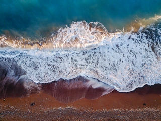 Fototapeta na wymiar Top photo view from flying drone of azure coral sea landscape with turquoise water and waves approaching the gravel beach.