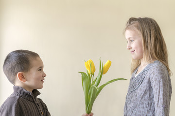 A cute little boy gives flowers to a girl who is older than him. The concept of love and friendship