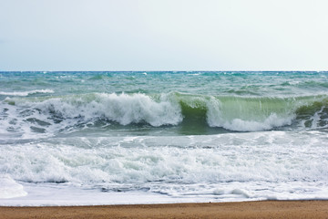 Stormy sea and blue sky, white sea foam on a yellow sandy beach.